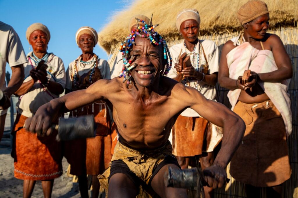 Khwai Villagers standing in a half circle with one man dancing and smiling at the front